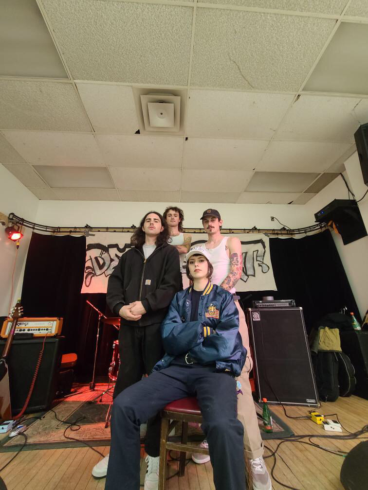 a fourpiece band of young people posing in their practice space looking tough